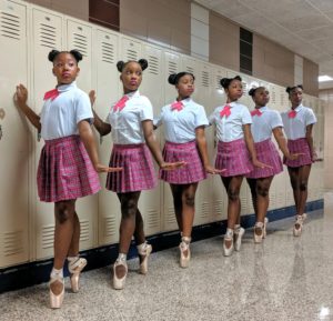 Dancers in matching outfits pose in school hallway.